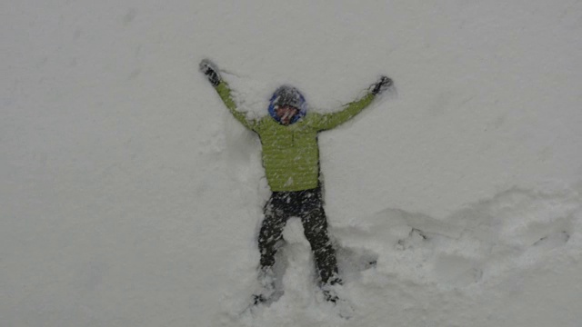 成年男子躺在刚下的雪中，做雪天使玩得很开心视频下载