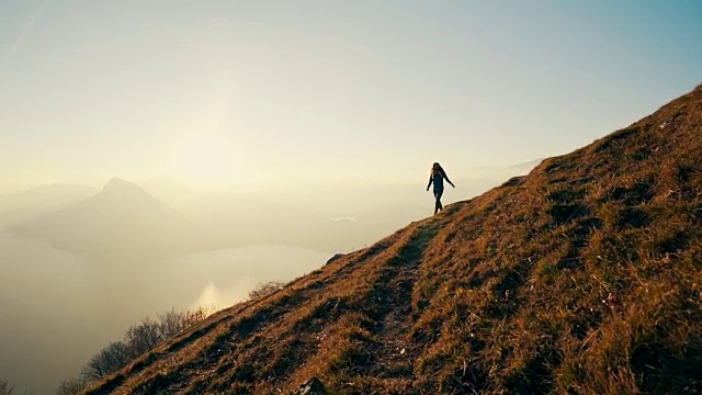 日落时分，女性徒步在湖上的高山草地上行走视频素材