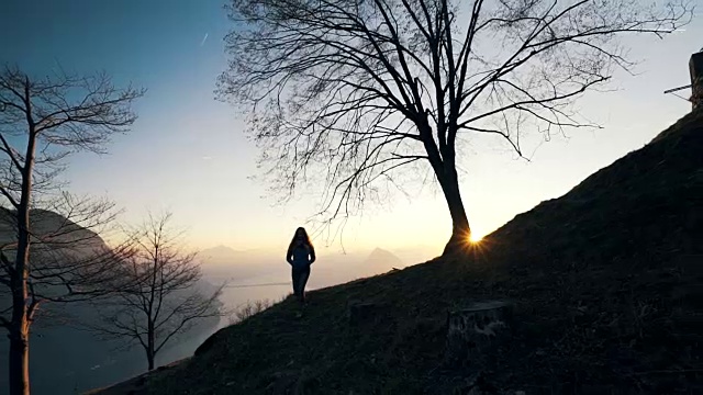 一个女人在日落时走在树下视频素材