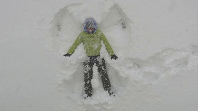 成年男子躺在刚下的雪中，做雪天使玩得很开心视频下载