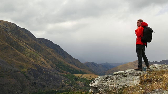 年轻人爬上岩石坡，望着远处有建筑风暴的山视频素材