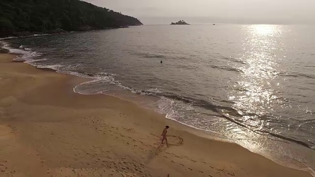 鸟瞰图的年轻女子在托克-托克Pequeno海滩的沙滩上画一个太阳形状视频素材