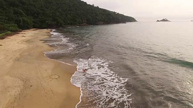 鸟瞰图的年轻女子在托克-托克Pequeno海滩的沙滩上画一个太阳形状视频素材