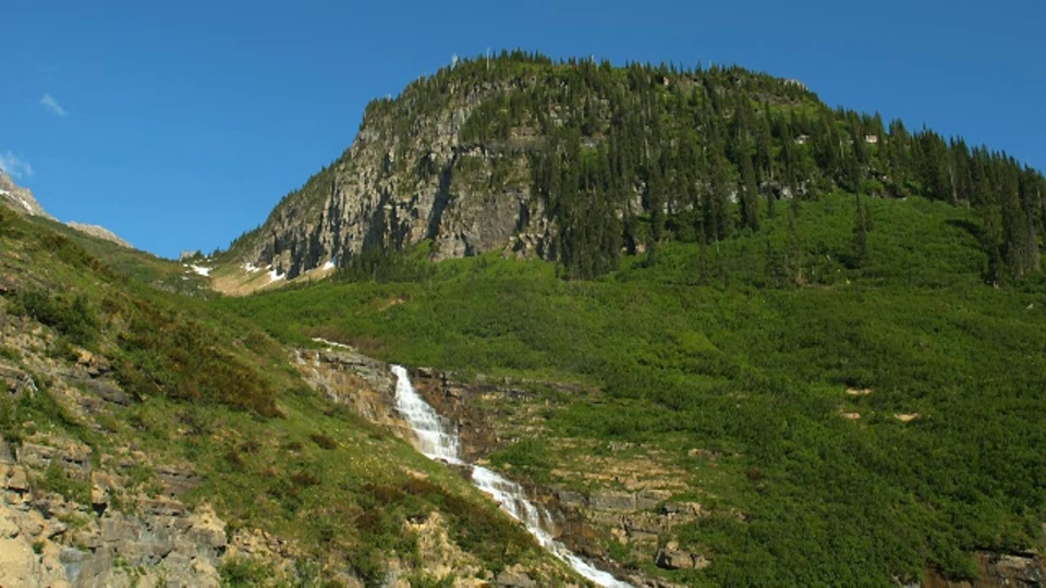 在冰川国家公园，一座岩石山高耸于瀑布之上。视频素材