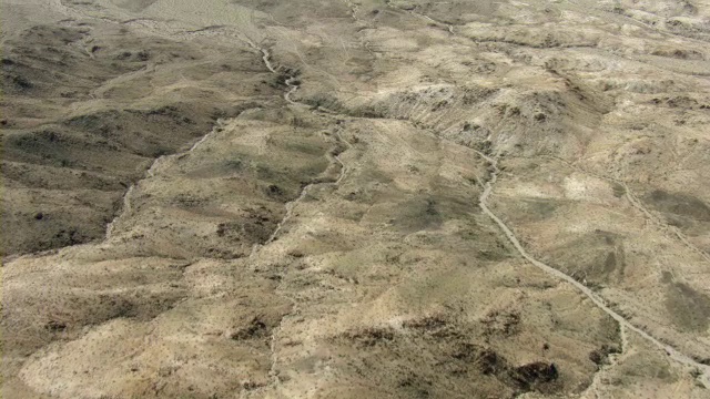 在广阔干旱的内华达州沙漠中，一条土路在高大坚硬的沙丘之间穿行。视频素材