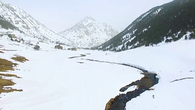 无人机拍摄的航拍镜头，在美丽的安道尔雪景上的冬天，蜿蜒的河流在雪谷中流淌，与美丽的对比和山峰。4 k UHD。视频素材