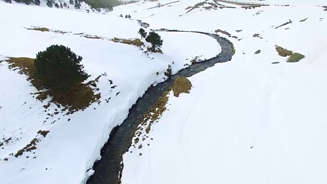 无人机拍摄的航拍镜头，在美丽的安道尔雪景上的冬天，蜿蜒的河流在雪谷中流淌，与美丽的对比和山峰。4 k UHD。视频素材