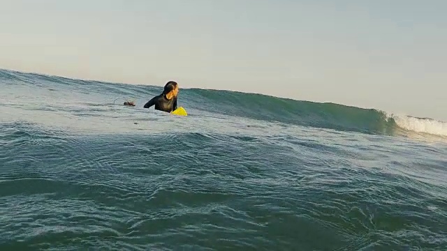 美丽的女性冲浪者坐在冲浪板上，海浪翻滚通过在荒凉的沙滩在法国南部大西洋海岸。视频素材