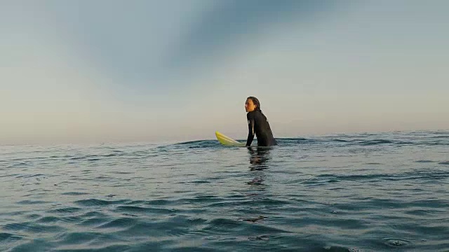 在法国南部大西洋海岸荒芜的沙滩上，女冲浪者坐在冲浪板上。视频素材