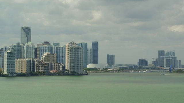 从空中掠过一片浅绿色的海面，海面上点缀着小船，遥望迈阿密的天际线视频素材