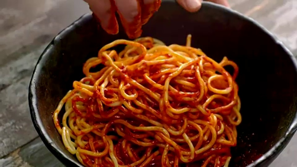 混合jjolmyeon(韩国面条)和gochujang(辣椒酱)(韩国流行菜Bibim guksu(混合面条))视频素材