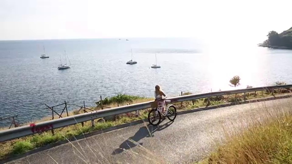 妇女骑着自行车在海上蜿蜒的乡村道路上行驶视频素材