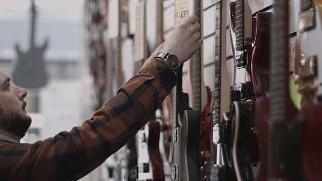 年轻的成年男子在商店定价吉他视频素材