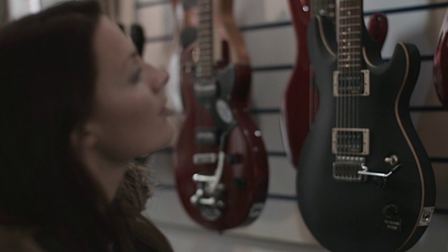 年轻的成年女性在商店看吉他视频素材