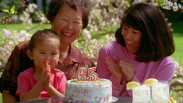 慢镜头中拍摄母亲在祖母和女儿吹灭生日蛋糕上的蜡烛时鼓掌视频素材