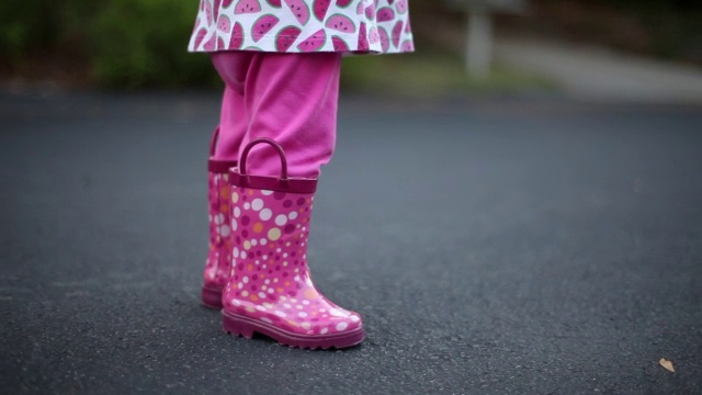 一个蹒跚学步的小女孩穿着粉红色雨靴在户外跳舞。视频素材