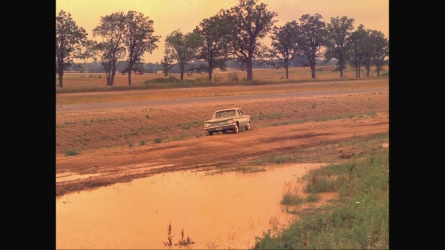 一名男子驾驶着一辆1960年的雪佛兰Corvair汽车在泥泞的道路上行驶，车被卡住了视频素材