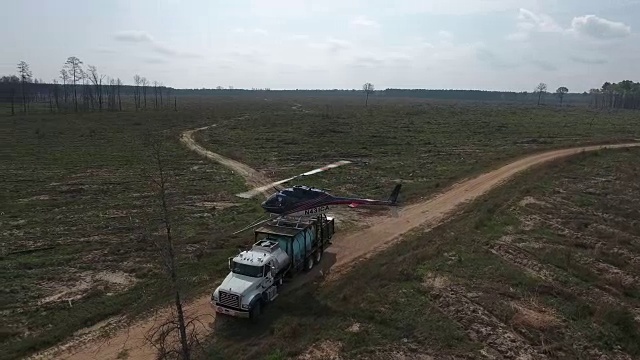 直升机对卡车的半轨道-无人机空中4K空中拍摄特技直升机对农作物和树木喷洒农药和杀虫剂，用于生产各种需要4K运输的农业视频素材