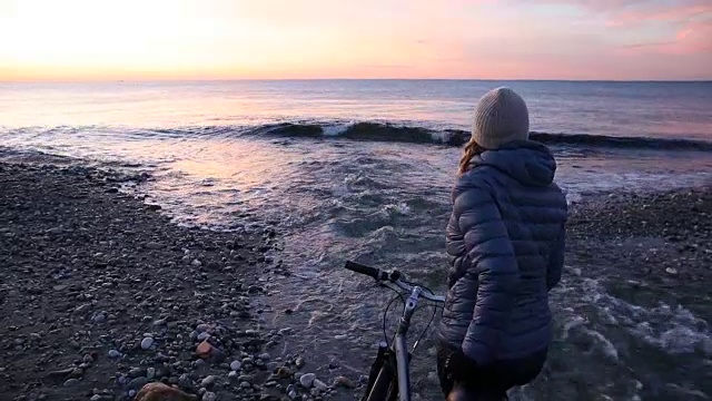 日出时分，一名女子在海滩河边推着自行车视频素材