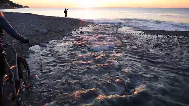 日出时分，一名女子在海滩河边推着自行车视频素材