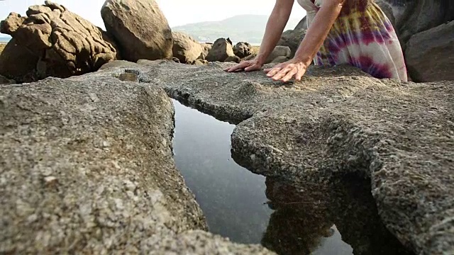 女人走在卵石之间，用手抚摸着水视频素材