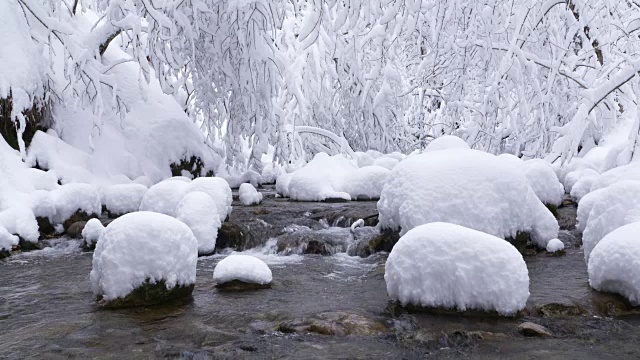 小溪在白雪覆盖的森林中飘雪。视频素材