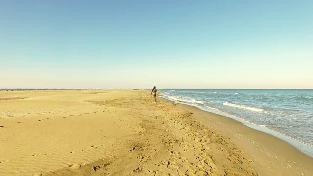 在加泰罗尼亚地区的周末旅行中，一名女孩在地中海和低浪的埃布罗三角洲海滩上散步和玩狗的视频是用无人机拍摄的。4 k UHD。视频素材