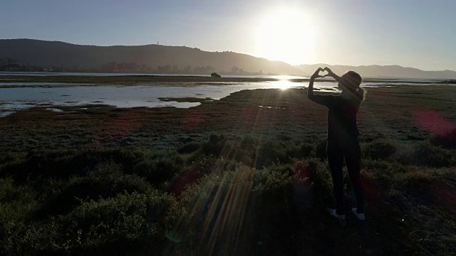 年轻女子在夕阳下做心形的指架视频素材