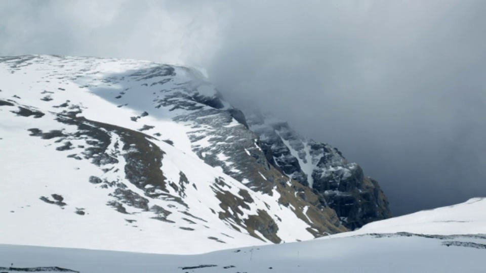 一层厚厚的灰色雾漂浮在白雪覆盖的岩石山顶上。视频素材