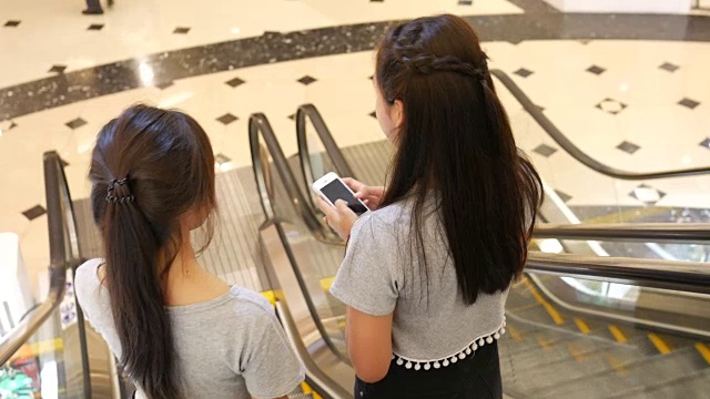 一对年轻女子在自动扶梯上使用智能手机视频素材