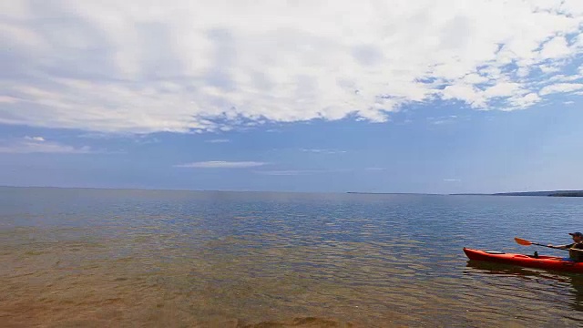 男孩划着皮划艇穿过苏必利尔湖，在阳光明媚的日子里用手划过清澈的湖水。视频素材