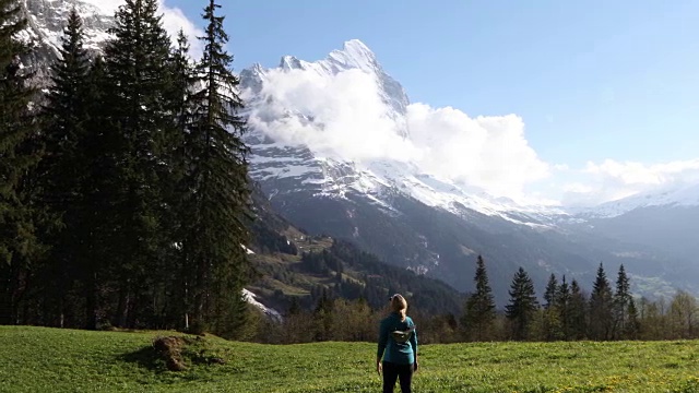 女徒步旅行者穿过雪山下的草地视频素材