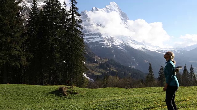 女徒步旅行者穿过雪山下的草地视频素材