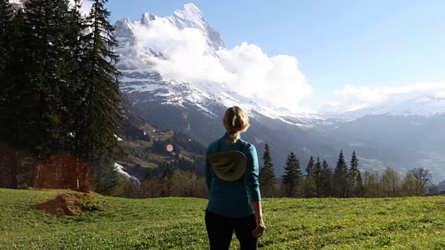 女徒步旅行者穿过雪山下的草地视频素材