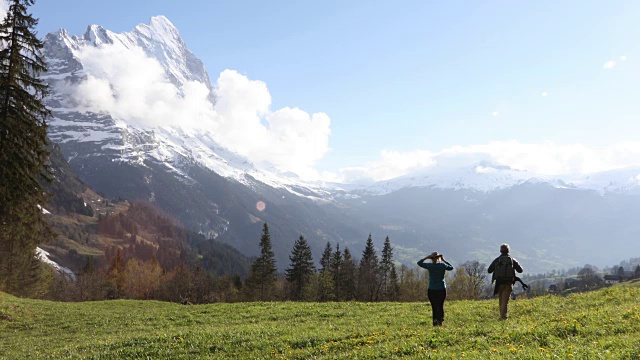 一对徒步夫妇穿过雪山下的草地视频素材