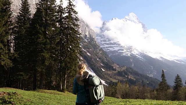 女徒步旅行者穿过雪山下的草地视频素材