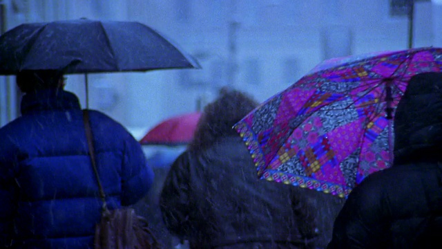 中镜头的人们，很多人撑着雨伞，走在城市的雪地上视频素材