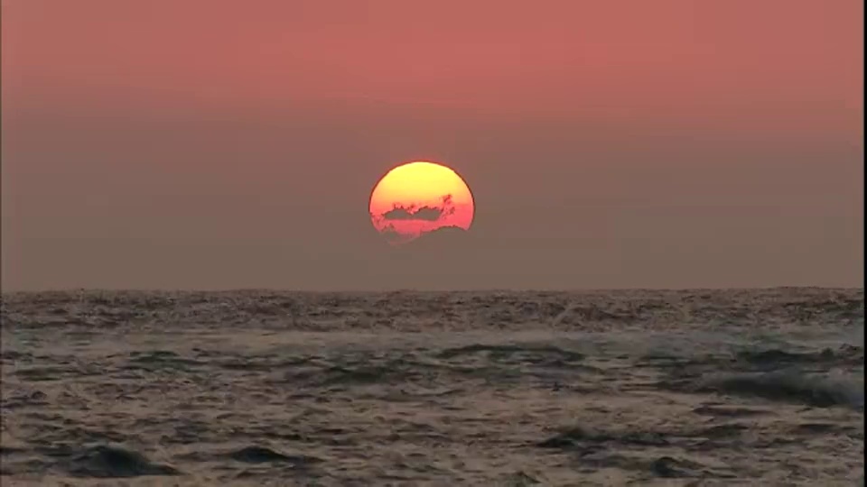 灰色的天空中，一颗黄色的大太阳悬在海洋的地平线上。视频素材