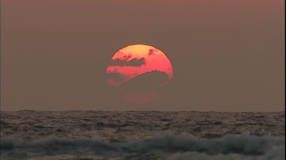 灰色的天空中，一颗黄色的大太阳悬在海洋的地平线上。视频素材