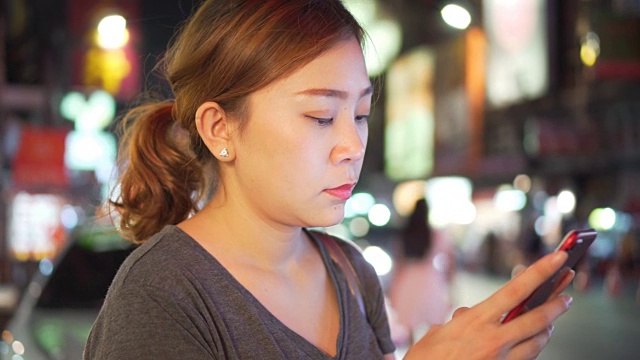 亚洲女孩在夜城的街道上使用手机视频素材