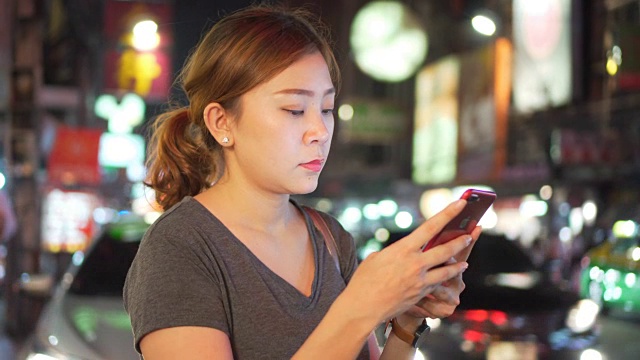 亚洲女孩在夜城的街道上使用手机视频素材