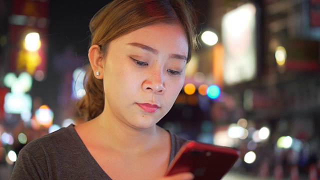 亚洲女孩在夜城的街道上使用手机视频素材