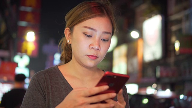 亚洲女孩在夜城的街道上使用手机视频素材