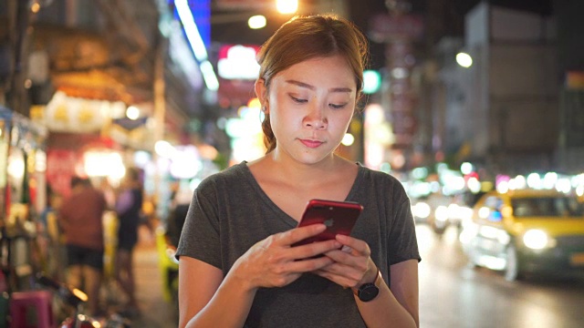 亚洲女孩在夜城的街道上使用手机视频下载