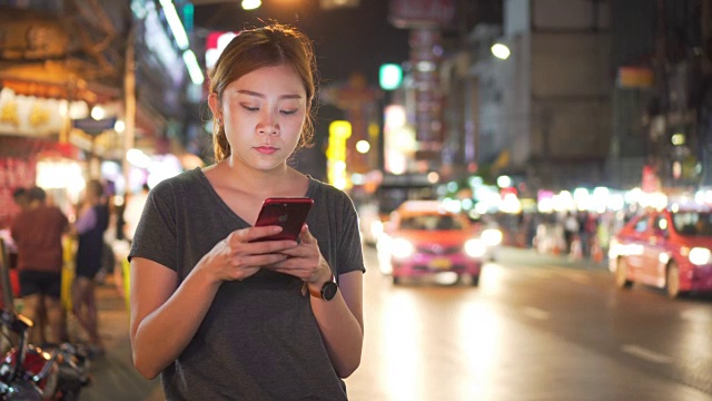 亚洲女孩在夜城的街道上使用手机视频下载