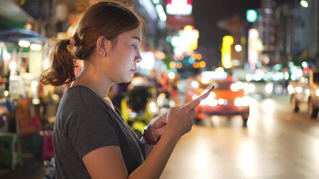 亚洲女孩在夜城的街道上使用手机视频下载