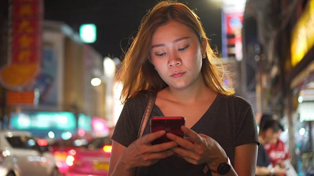 亚洲女孩在夜城的街道上使用手机视频下载