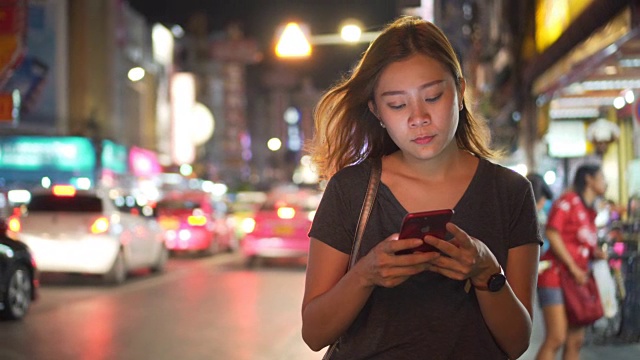 亚洲女孩在夜城的街道上使用手机视频下载