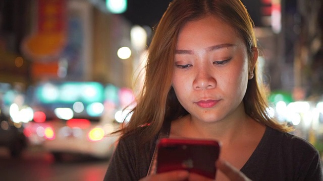 亚洲女孩在夜城的街道上使用手机视频素材