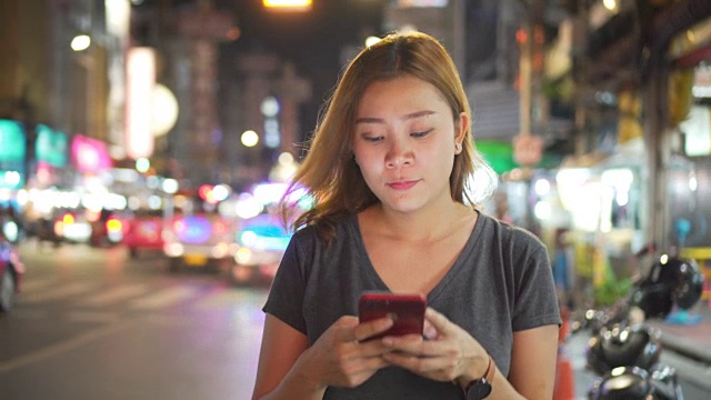 亚洲女孩在夜城的街道上使用手机视频素材